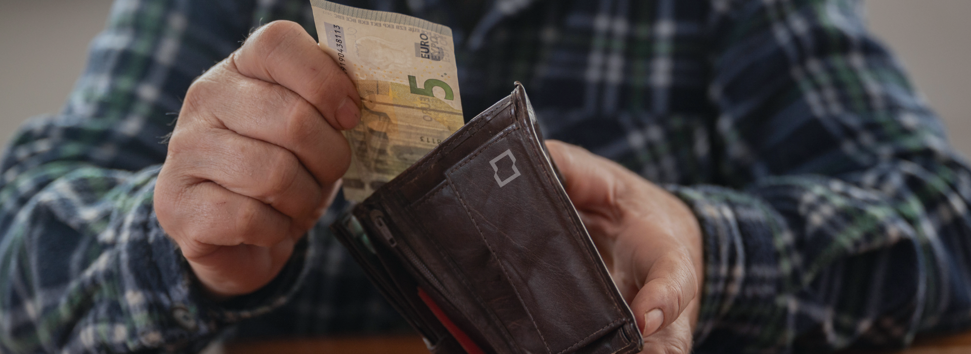 Starší človek vyberá peniaze z peňaženky ako symbol rodičovského dôchodku a finančného príspevku pre rodičov v roku 2026.